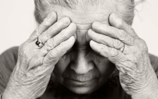 black and white senior aged person holding their head in their hands